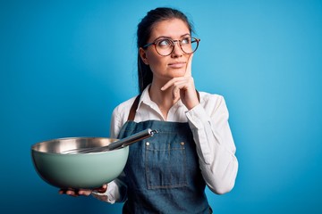 Young beautiful cooker woman with blue eyes using bowl and whisk over isolated background serious...
