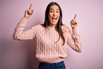 Young beautiful brunette woman wearing casual sweater over isolated pink background smiling amazed and surprised and pointing up with fingers and raised arms.