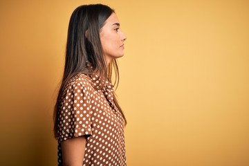 Young beautiful brunette woman wearing casual shirt over isolated yellow background looking to...