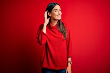 Young beautiful brunette woman wearing casual sweater over isolated red background smiling with...