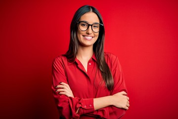 Young beautiful brunette woman wearing casual shirt and glasses over red background happy face...
