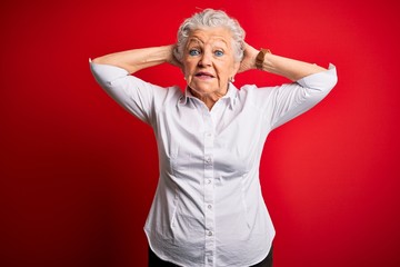 Senior beautiful woman wearing elegant shirt standing over isolated red background Crazy and scared with hands on head, afraid and surprised of shock with open mouth