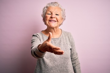 Senior beautiful woman wearing casual t-shirt standing over isolated pink background smiling friendly offering handshake as greeting and welcoming. Successful business. © Krakenimages.com