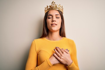 Young beautiful brunette woman wearing golden queen crown over white background smiling with hands...