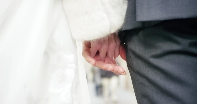 Close-up of a bride and groom's hands intertwined as they wait to cross the street