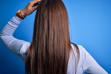 Young beautiful brunette woman wearing casual sweater standing over blue background Backwards thinking about doubt with hand on head