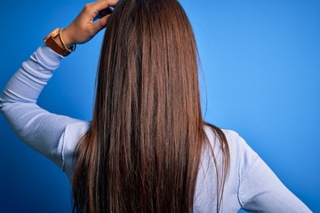 Fototapeta premium Young beautiful brunette woman wearing casual sweater standing over blue background Backwards thinking about doubt with hand on head