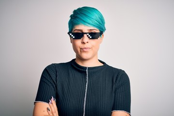 Young woman with blue fashion hair wearing thug life sunglasses over white background skeptic and nervous, disapproving expression on face with crossed arms. Negative person.