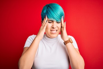 Young beautiful woman with blue fashion hair wearing casual t-shirt over red background with hand on headache because stress. Suffering migraine.