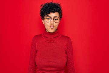 Obraz premium Young beautiful african american afro woman wearing turtleneck sweater and glasses making fish face with lips, crazy and comical gesture. Funny expression.