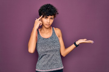 Young beautiful african american afro sportswoman doing exercise wearing sportswear confused and annoyed with open palm showing copy space and pointing finger to forehead. Think about it.