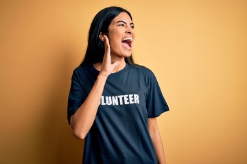 Young beautiful hispanic woman wearing volunteer t-shirt as social charity moral shouting and...