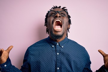 Young handsome african american man wearing casual shirt and glasses over pink background crazy and...