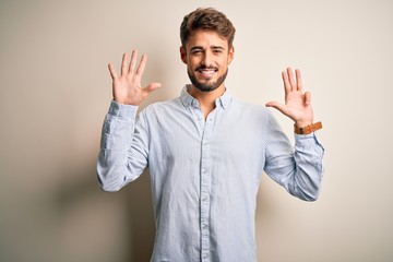 Young handsome man with beard wearing striped shirt standing over white background showing and pointing up with fingers number nine while smiling confident and happy.