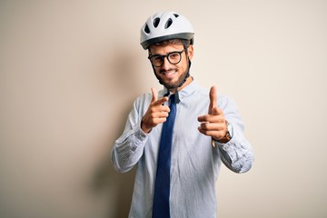 Young businessman wearing glasses and bike helmet standing over isolated white bakground pointing fingers to camera with happy and funny face. Good energy and vibes.