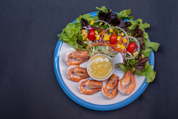 Shrimpand salad of fresh vegetables close-up on a plate on black background. horizontal view from above