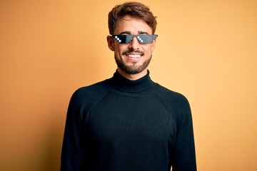 Young man wearing thug life fanny sunglasses standing over isolated yellow background with a happy and cool smile on face. Lucky person.
