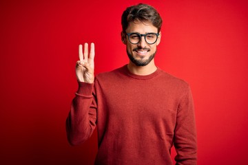 Young handsome man with beard wearing glasses and sweater standing over red background showing and...