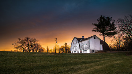 Panoramic view of a  white barn in a public park beneath a stirring rural sunrise