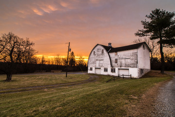 Fototapeta na wymiar A white barn in a public park during a colorful country sunrise