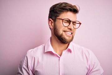 Obraz premium Young handsome blond man with beard and blue eyes wearing pink shirt and glasses with hand on stomach because nausea, painful disease feeling unwell. Ache concept.
