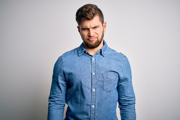 Young handsome blond man with beard and blue eyes wearing casual denim shirt skeptic and nervous,...