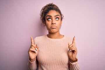Young beautiful african american girl wearing casual sweater standing over pink background Pointing...