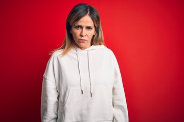 Middle age beautiful sportswoman wearing casual sweatshirt over isolated red background skeptic and...