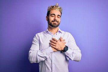 Young handsome man with beard wearing golden crown of king over purple background smiling with...