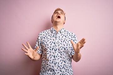 Young handsome redhead man wearing casual summer shirt standing over pink background crazy and mad...