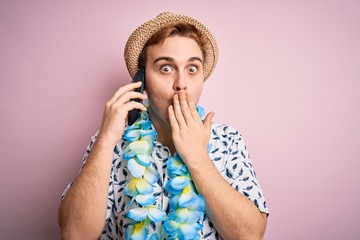Young man on vacation wearing hat and hawaiian lei having conversation talking on smartphone...