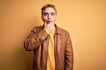 Young handsome redhead man wearing casual leather jacket over isolated yellow background Looking fascinated with disbelief, surprise and amazed expression with hands on chin