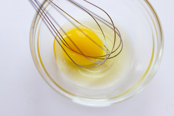 Closeup of metal whisk and chicken yolk in a glass bowl