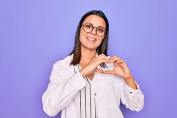 Young beautiful brunette psychologist woman wearing coat and glasses over purple background smiling...