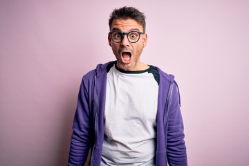 Obraz premium Young handsome man wearing purple sweatshirt and glasses standing over pink background afraid and shocked with surprise and amazed expression, fear and excited face.