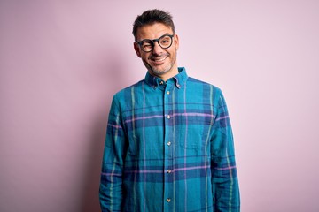 Young handsome man wearing casual shirt and glasses standing over isolated pink background winking looking at the camera with sexy expression, cheerful and happy face.