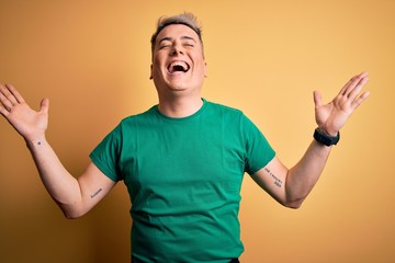 Fototapeta premium Young handsome modern man wearing casual green t-shirt over yellow background celebrating mad and crazy for success with arms raised and closed eyes screaming excited. Winner concept