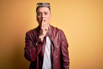 Young handsome modern man wearing fashion leather jacket and sunglasses over yellow background asking to be quiet with finger on lips. Silence and secret concept.