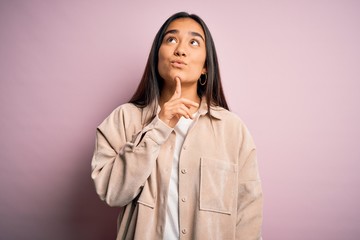 Young beautiful asian woman wearing casual shirt standing over pink background Thinking concentrated about doubt with finger on chin and looking up wondering