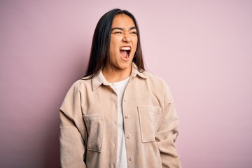 Young beautiful asian woman wearing casual shirt standing over pink background angry and mad screaming frustrated and furious, shouting with anger. Rage and aggressive concept.