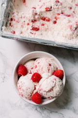 A pretty bowl of strawberry ice cream scoops with a metal tray of ice cream.