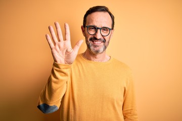 Middle age hoary man wearing casual sweater and glasses over isolated yellow background showing and pointing up with fingers number five while smiling confident and happy.