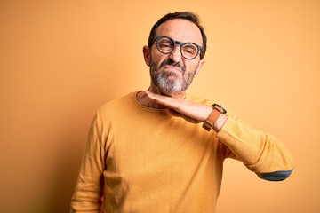 Middle age hoary man wearing casual sweater and glasses over isolated yellow background cutting throat with hand as knife, threaten aggression with furious violence
