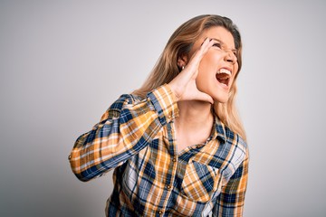 Young beautiful blonde woman wearing casual shirt standing over isolated white background shouting and screaming loud to side with hand on mouth. Communication concept.