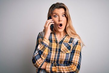 Beautiful blonde woman having conversation talking on the smartphone over white background scared...