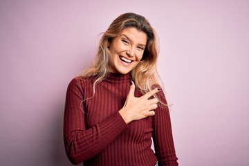 Fototapeta premium Young beautiful blonde woman wearing casual sweater over isolated pink background cheerful with a smile of face pointing with hand and finger up to the side with happy and natural expression on face