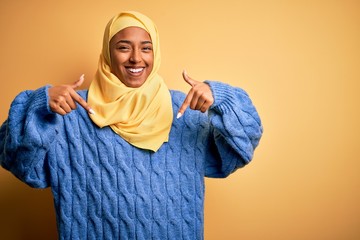 Young African American afro woman wearing muslim hijab over isolated yellow background looking confident with smile on face, pointing oneself with fingers proud and happy.