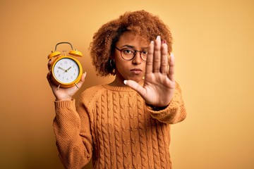 Young beautiful African American afro woman with curly hair holding vintage alarm clock with open...