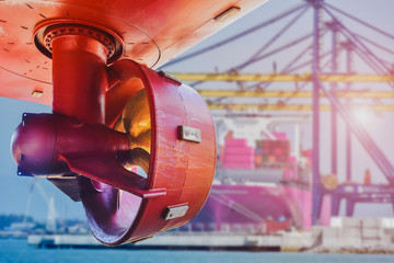 Red propeller in rope guard with rudder under Ship repairing in shipyard near port and crane lifting loading cargo container in port background. © TawanSaklay
