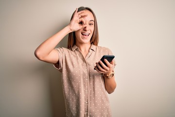 Young beautiful woman having conversation using smartphone looking at the mobile with happy face smiling doing ok sign with hand on eye looking through fingers